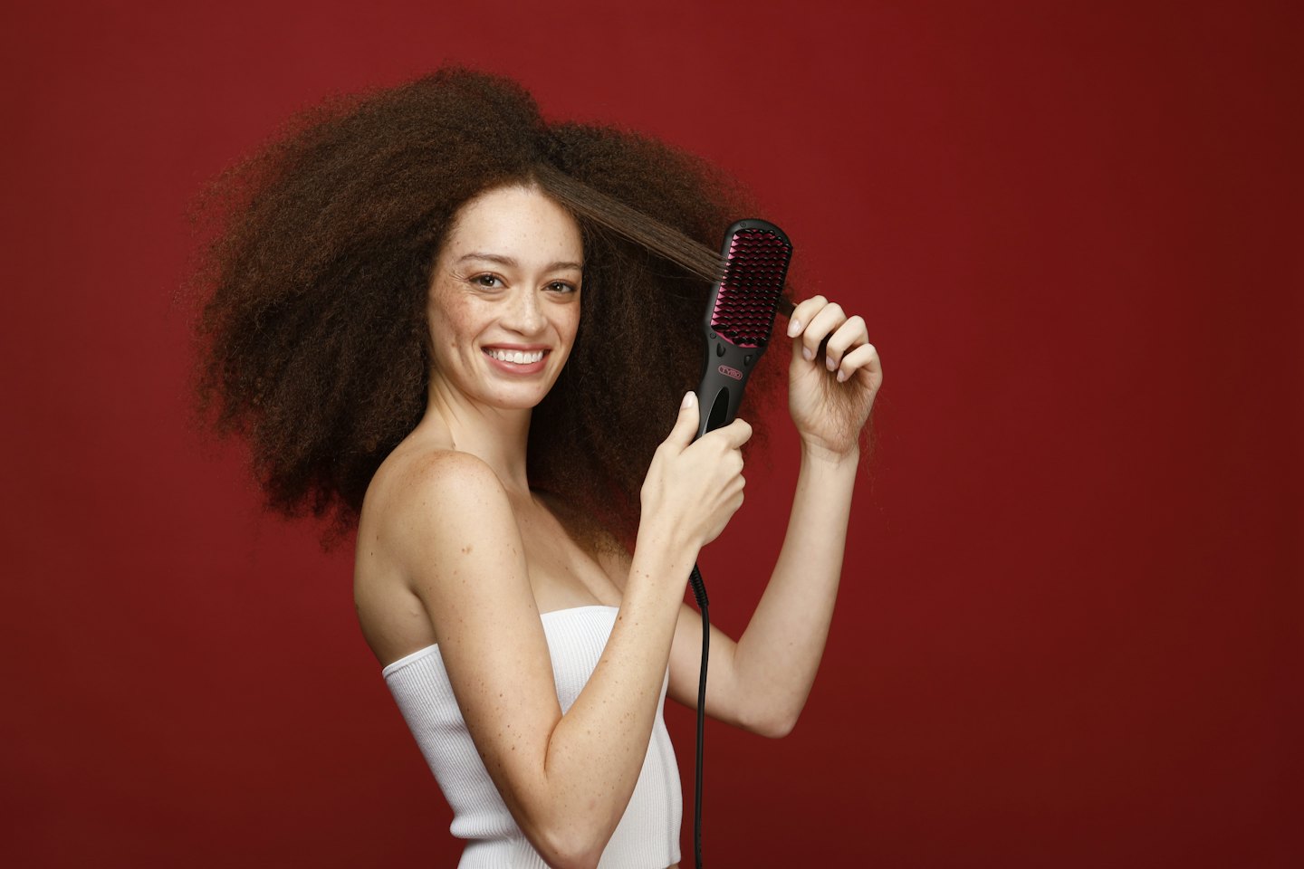 Young woman happily uses a pink and black hair straightening brush.